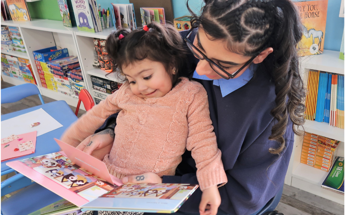 CIW dice el Día de sus hijos y muestra que las madres y los niños se unen con el libro, incluida esta madre con su hijo pequeño sentado en su regazo.